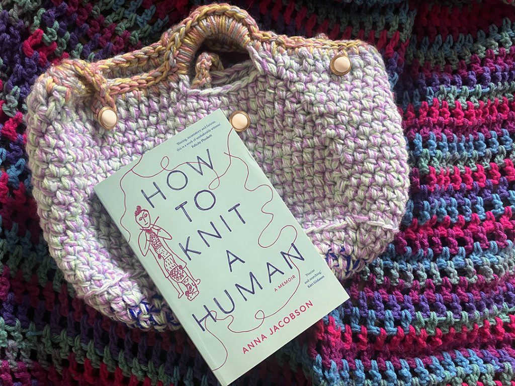 A knitted handbag on a knitted rug, with Anna's copy of How to Knit a Human